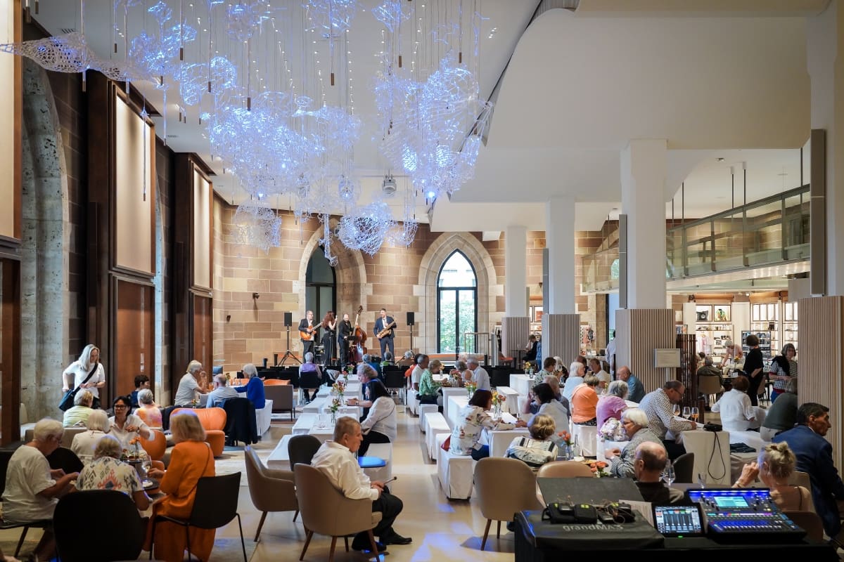 Mitglieder der Fördergesellschaft sitzen in der Dürnitz auf Loungemöbeln und an Tischen. Auf der Bühne im Hintergrund spielt eine Band.